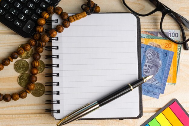 A close-up image of a hand writing in a budget notebook with the Colombian flag in the background. The image emphasizes financial planning.