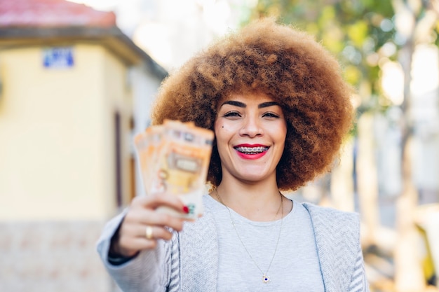 An image of a woman smiling while checking her bank balance on her smartphone, with a background of Colombian currency.