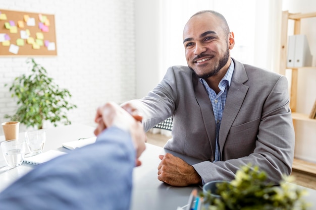 A Colombian businessman shaking hands with a financial advisor in an office setting. They are smiling confidently, suggesting a positive outcome of debt negotiation.