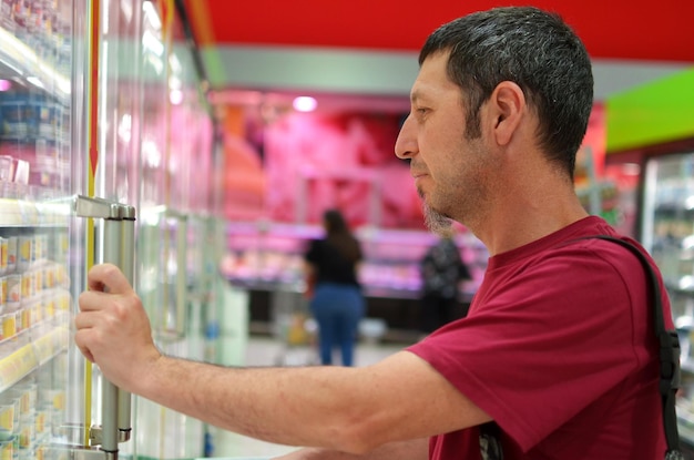 A person is holding a handful of Colombian pesos, looking concerned while standing in front of a grocery store with rising prices displayed on the windows.