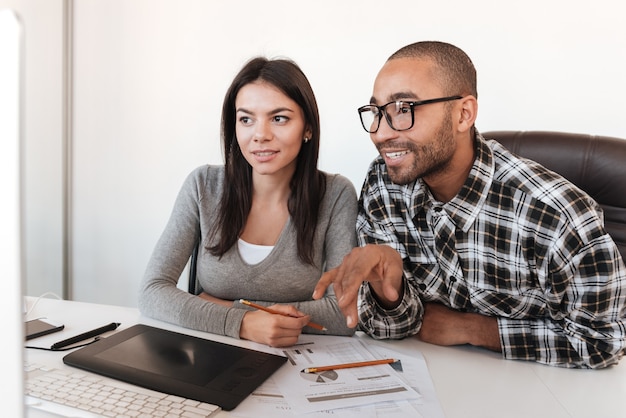 A young Colombian couple discussing insurance options with a financial advisor in a modern office setting. The advisor is using a tablet to show them different policy options, and the couple appears engaged and thoughtful.