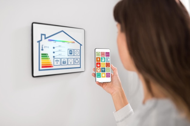 A close-up of a smart thermostat displaying energy usage statistics and settings, symbolizing energy efficiency and home automation. The thermostat is mounted on a wall in a modern living room, with sunlight streaming in.