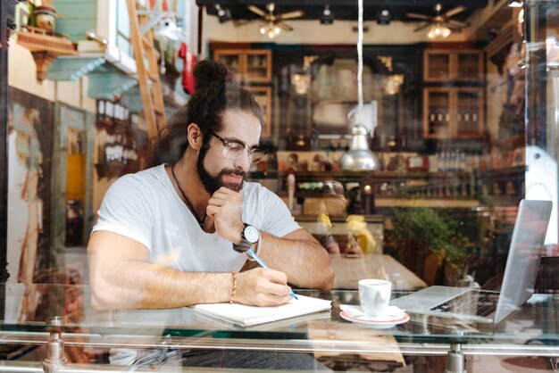 A small business owner in a local coffee shop reviewing financial documents with a pen and calculator, surrounded by stacks of paperwork and a laptop displaying a spreadsheet. Concentrate on the person's focused expression.