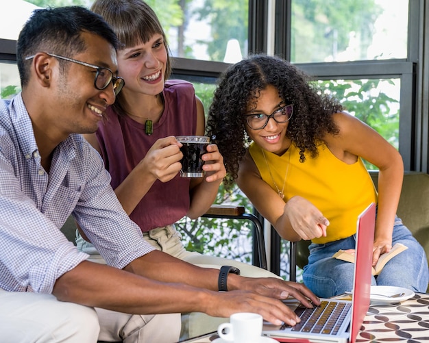 A team of young professionals in a coworking space in Bogotá, Colombia, collaborating on a digital project. They are using laptops and smartphones, with project management software visible on one of the screens.
